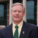 Smiling headshot of John Wood on campus in suit and tie